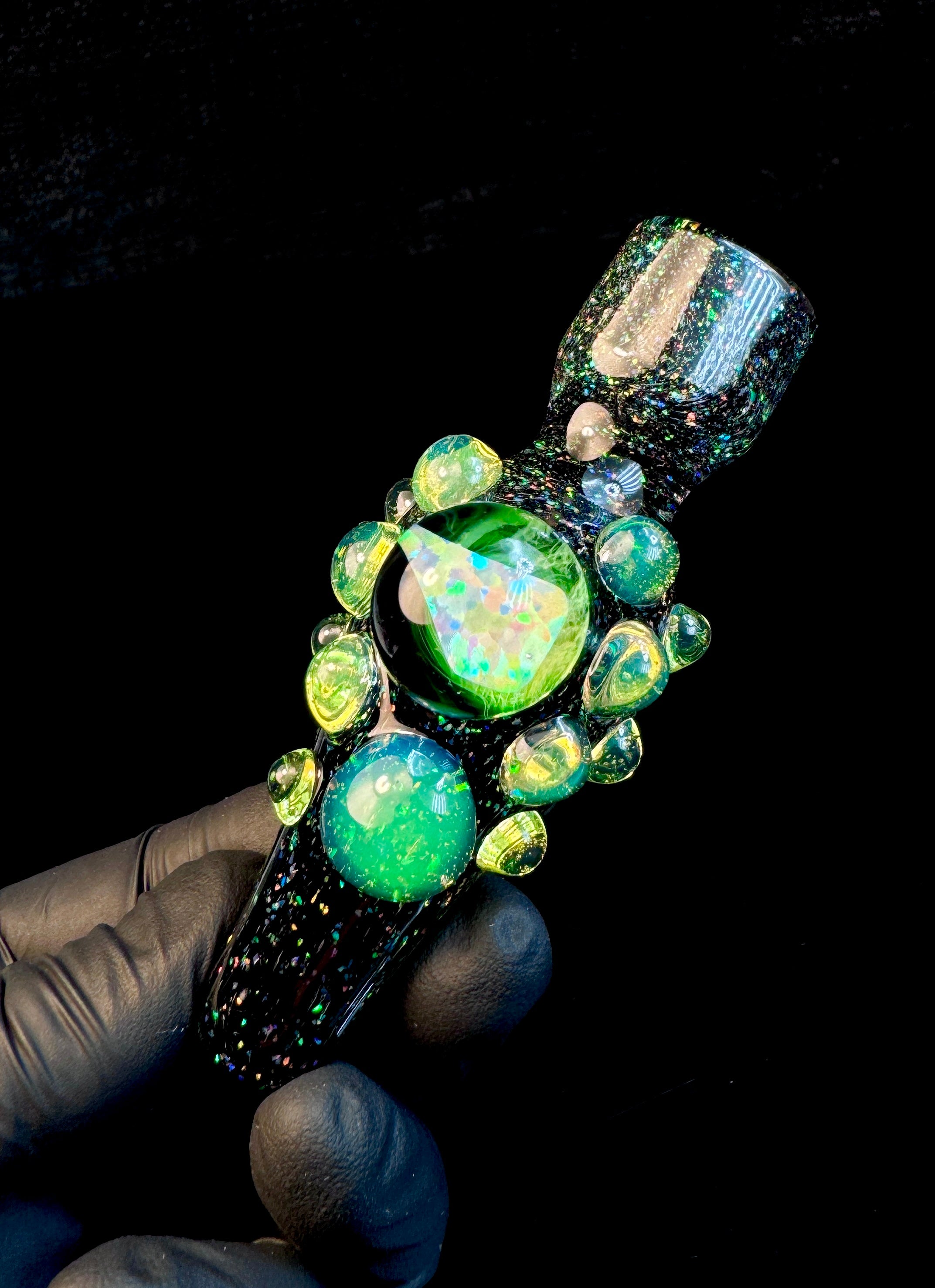 A hand holding a black crushed opal chillum pipe with slyme dots